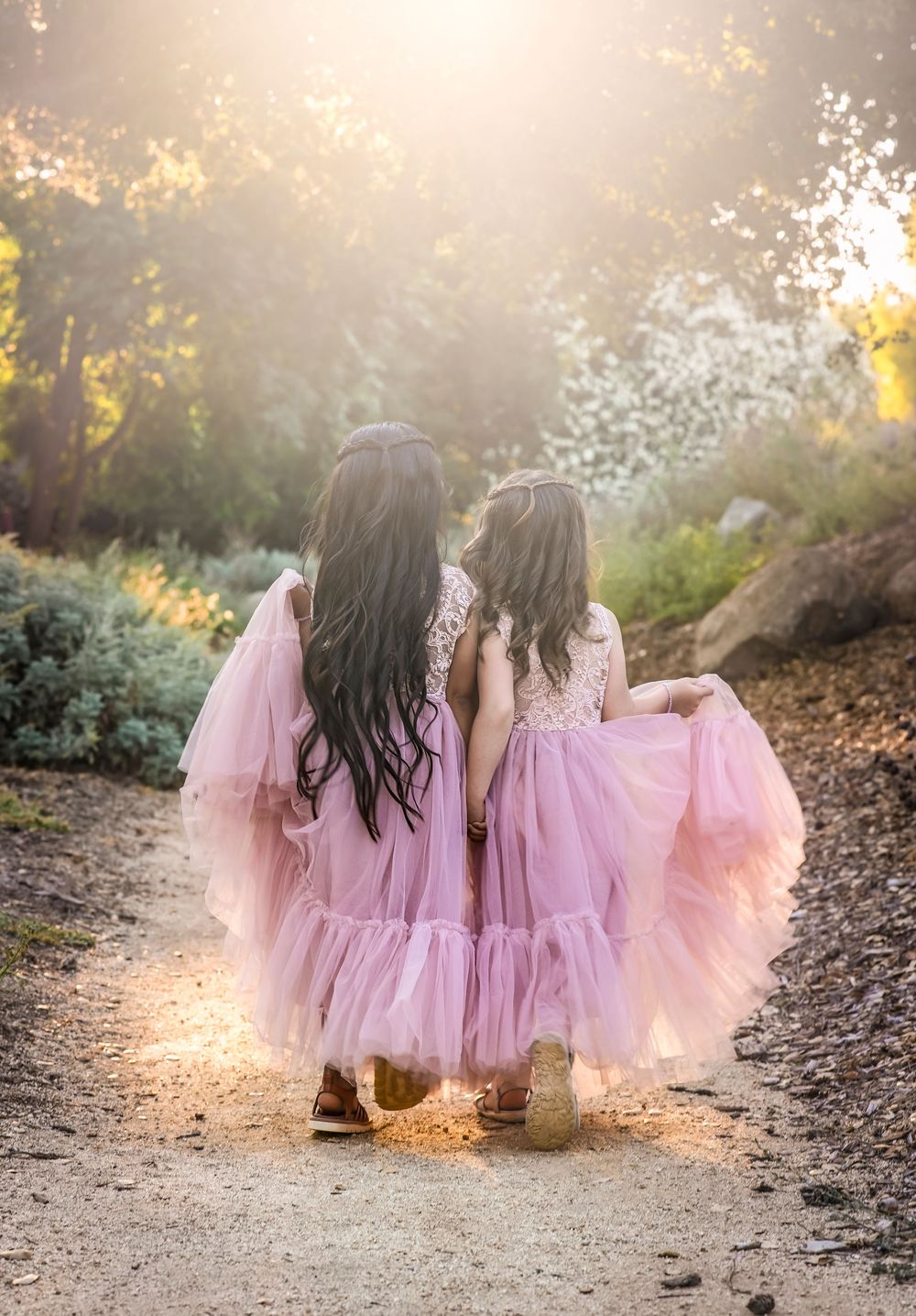 Two young girls in matching pink tulle dresses walk hand-in-hand down a sunlit garden path.
photographed by solstice&willow photography
