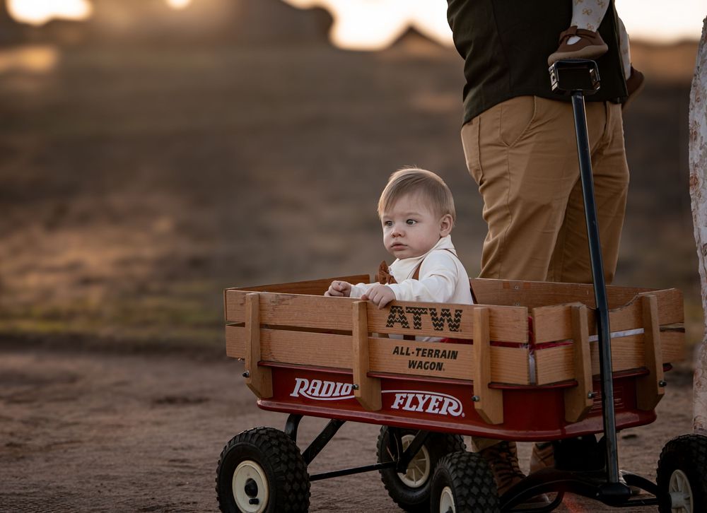 Baby sitting in a red Radio Flyer ATW All-Terrain Wagon outdoors at golden hour. Ramona grasslands Solstice & Willow photography