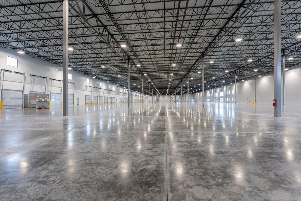 A vast, empty warehouse with a polished concrete floor, high ceilings supported by numerous pillars.