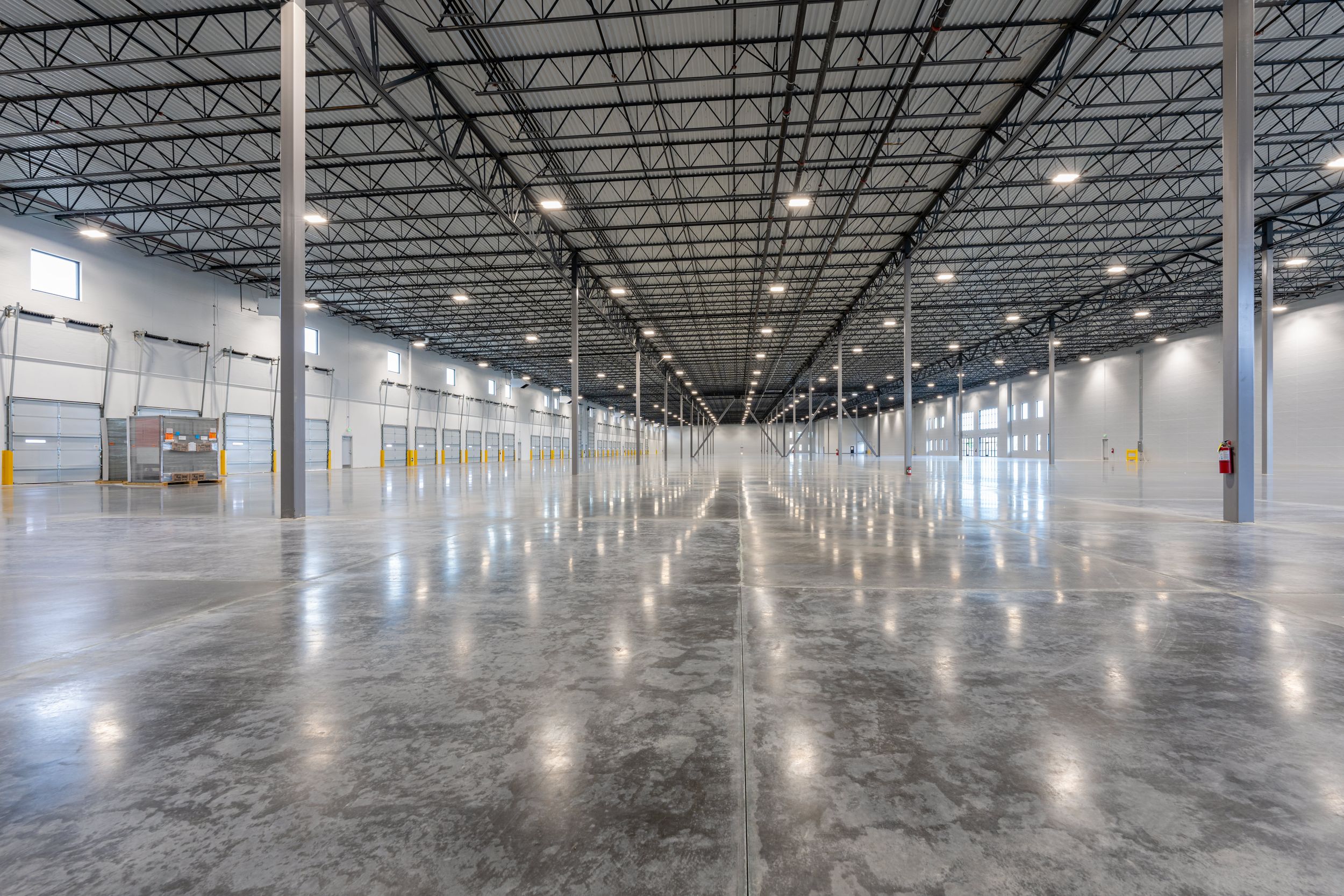 A vast, empty warehouse with a polished concrete floor, high ceilings supported by numerous pillars.