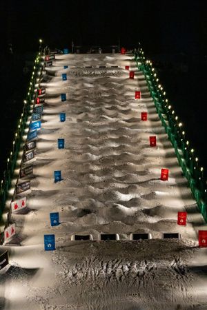 A well-lit ski slope at night, set up for a mogul competition. The slope is lined with evenly spaced moguls.