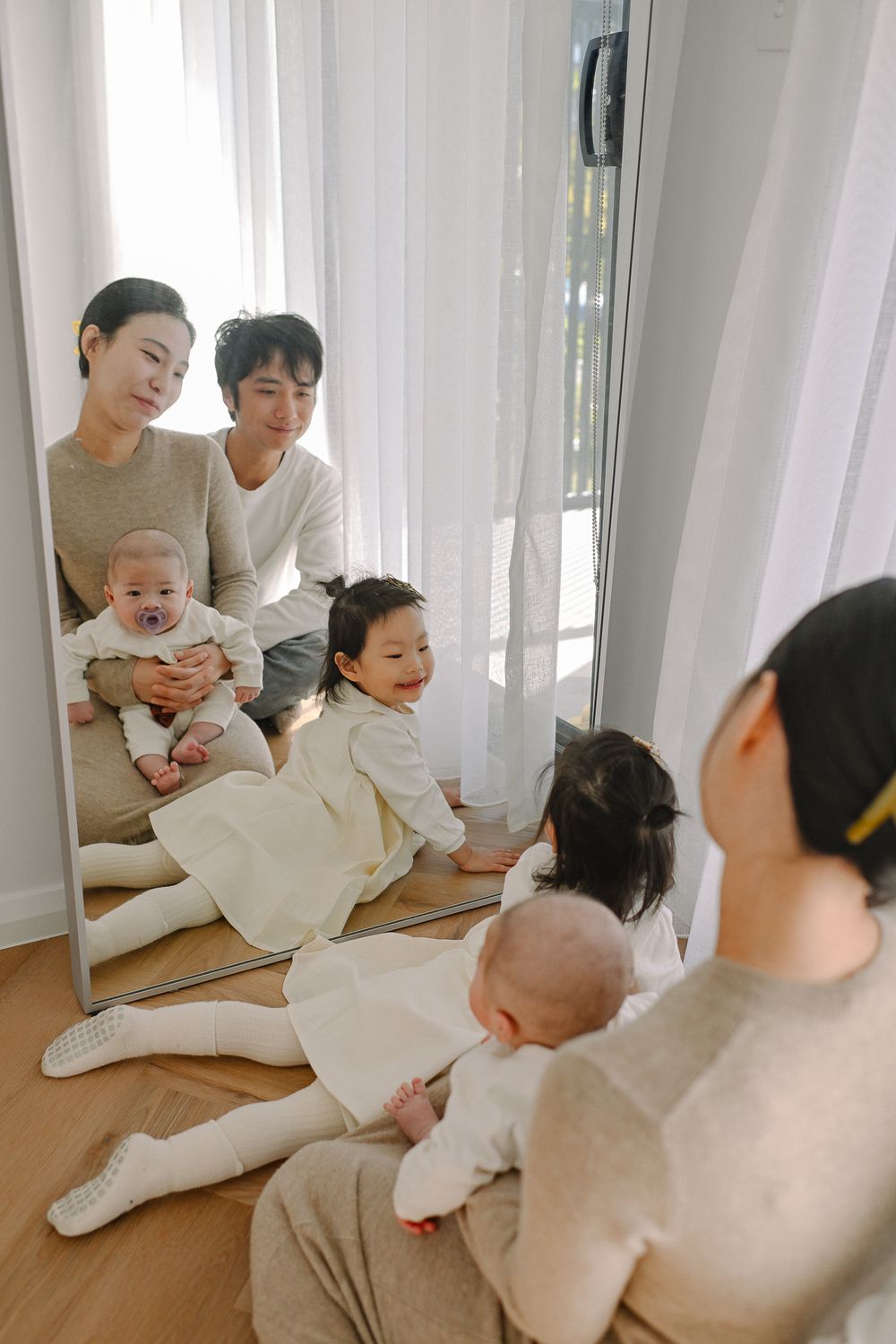 Family spending quality time together on a hardwood floor with white curtains in the background.