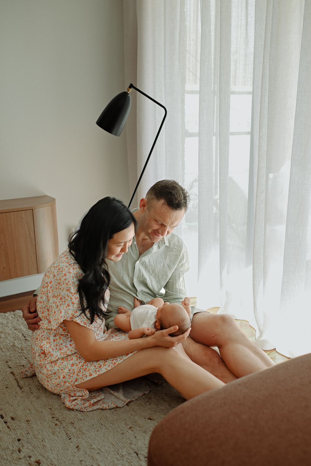 Two people lounging together on a carpeted floor near a bright window in a cozy indoor setting.