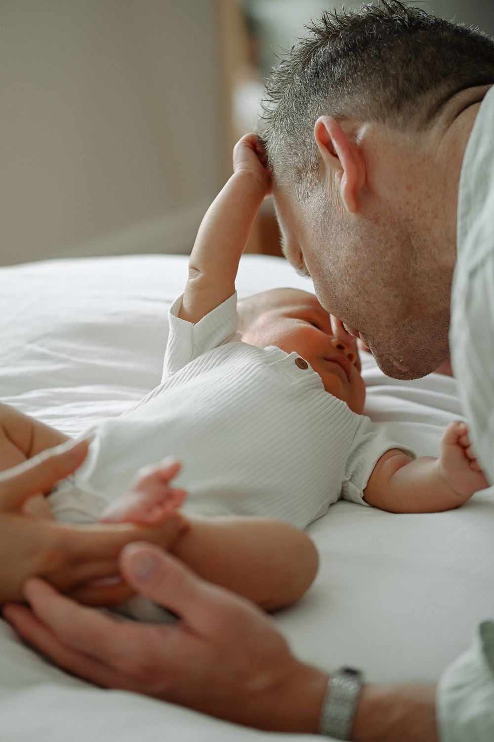 Tender moment between parent and newborn baby lying together on white bedding.