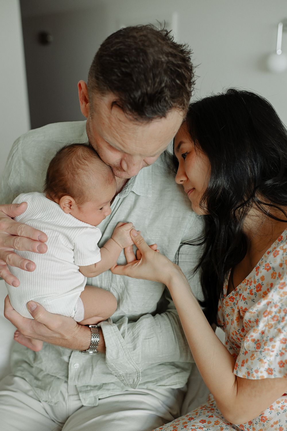 Parents sharing intimate bonding moments with their newborn baby on white bed linens.