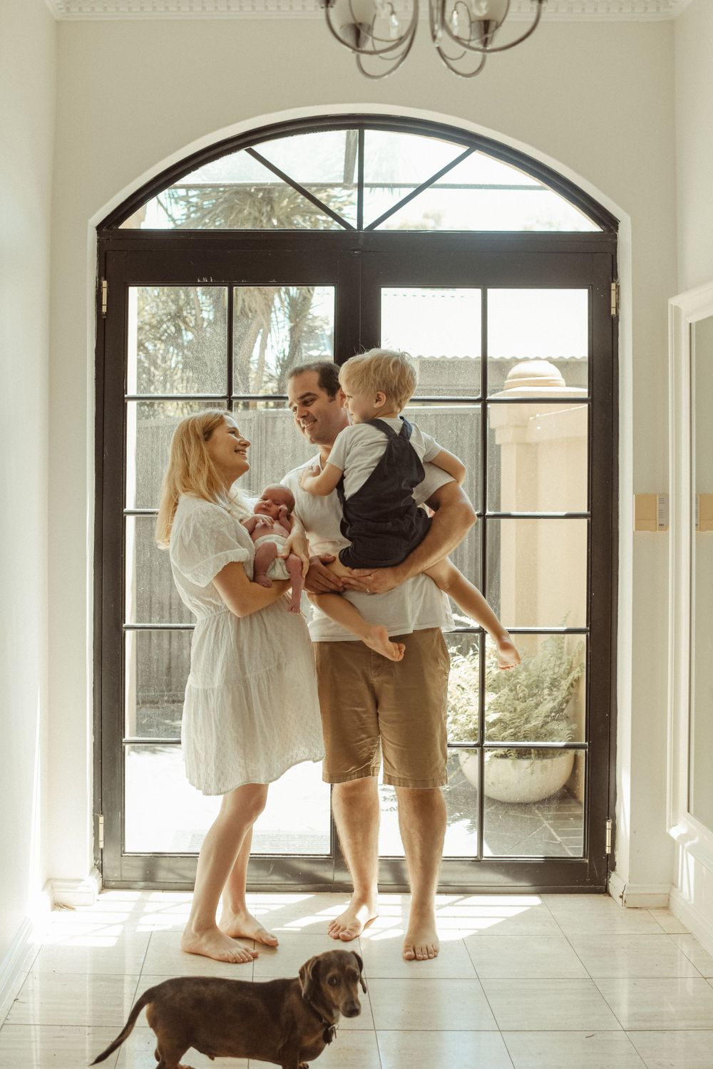 A family poses with their dog in front of large arched doors in a bright entryway.