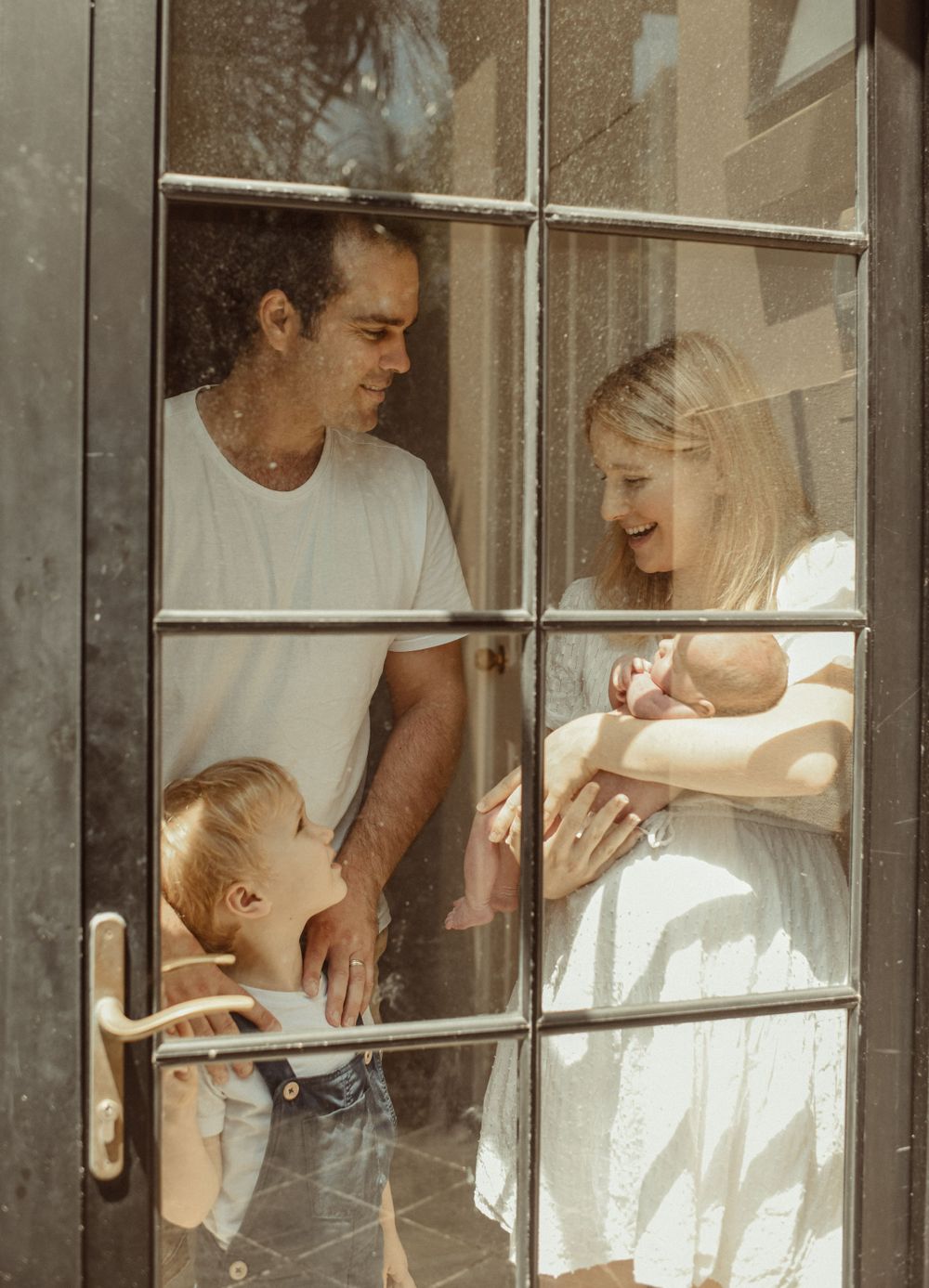 Through window panes, a family shares intimate moments with their children in natural light.