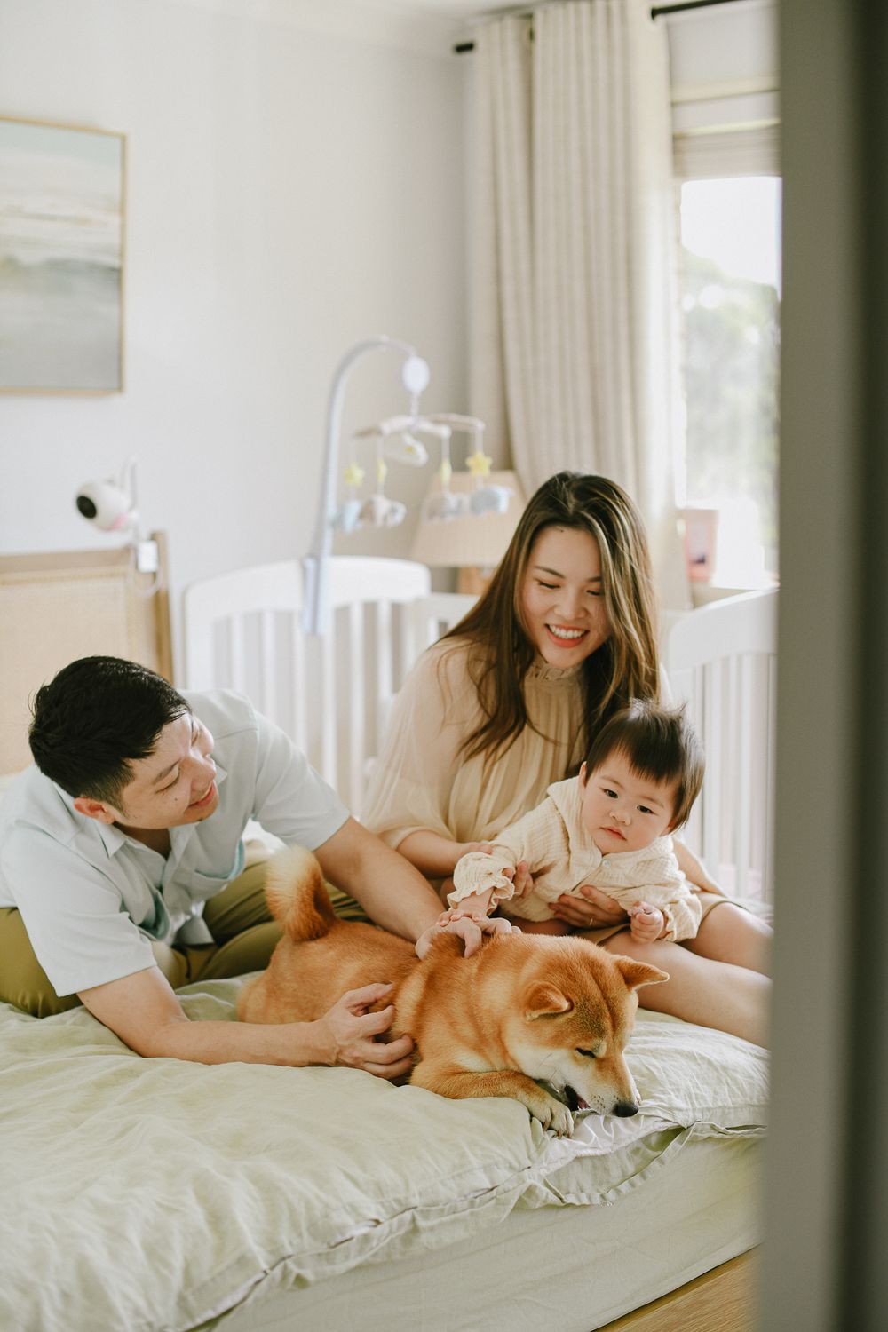 A family relaxes on a white bed with their Shiba Inu dog in a bright modern bedroom.