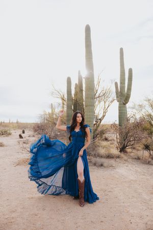 A flowing sapphire dress creates elegant movement against a desert backdrop with saguaro cacti.