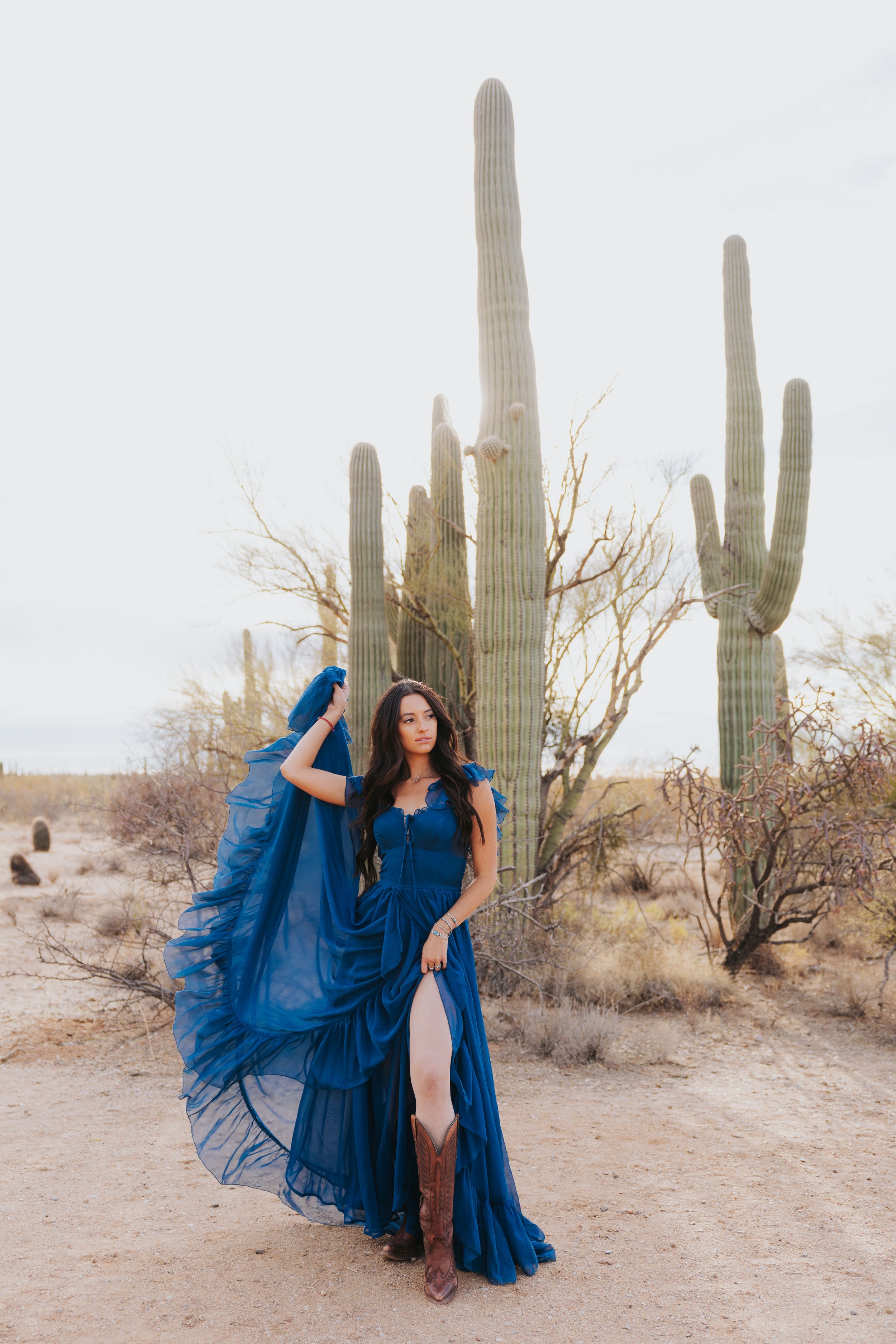 A flowing royal blue dress twirls gracefully against a backdrop of majestic saguaro cacti in the desert.