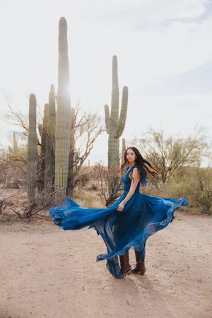 A royal blue gown swirls dramatically in a desert setting surrounded by towering saguaro cacti.