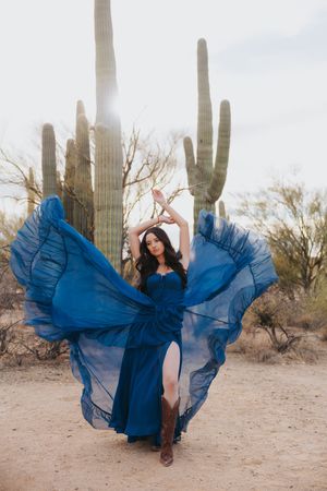 A flowing blue dress twirls gracefully against a desert backdrop with tall saguaro cacti.