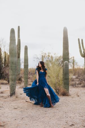 A flowing navy dress creates movement in a desert setting with towering saguaro cacti.