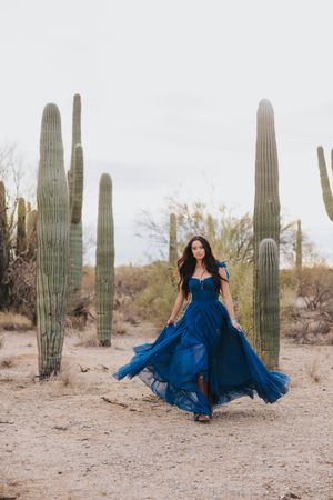 A royal blue gown swirls through the desert landscape surrounded by majestic saguaros.