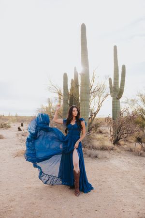A dramatic blue dress billows in the wind among desert saguaros during a photoshoot.