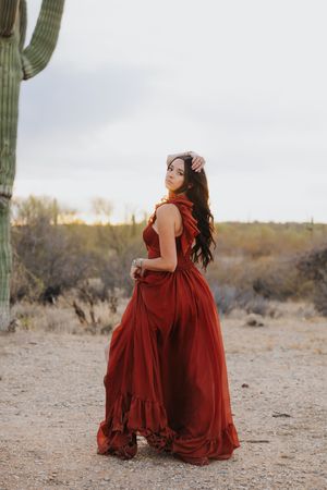 Dramatic fashion pose in a flowing red gown amidst desert cacti and brush.