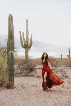 A crimson gown flows dramatically through a desert scene with tall saguaro cacti.