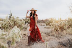 Wide-brimmed hat and red dress create romantic desert fashion scene among cacti.