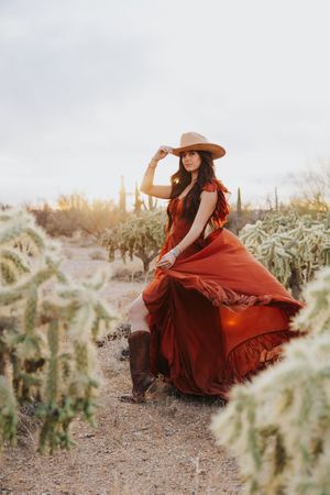 A flowing red dress twirls dramatically against a desert landscape with cacti at sunset.
