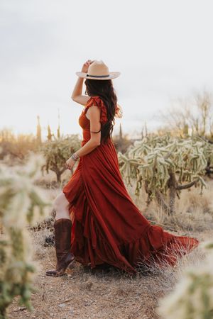 A flowing burgundy dress catches the wind among desert cacti and rocky terrain.