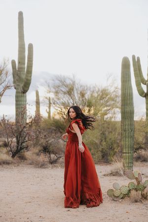A flowing red dress twirls gracefully among tall saguaro cacti in a desert landscape at sunset.
