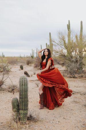 Dramatic red gown flows in the wind against a backdrop of desert cacti and scrubland.