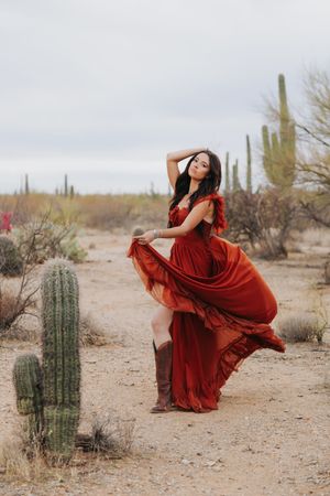 A flowing crimson dress creates elegant movement against the stark desert landscape with saguaros.