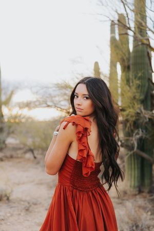Ethereal portrait in a red ruffled dress set against towering saguaro cacti in the desert.