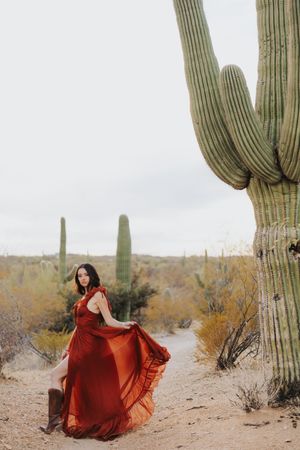 Billowing red dress creates striking contrast against majestic saguaro cacti in the desert.
