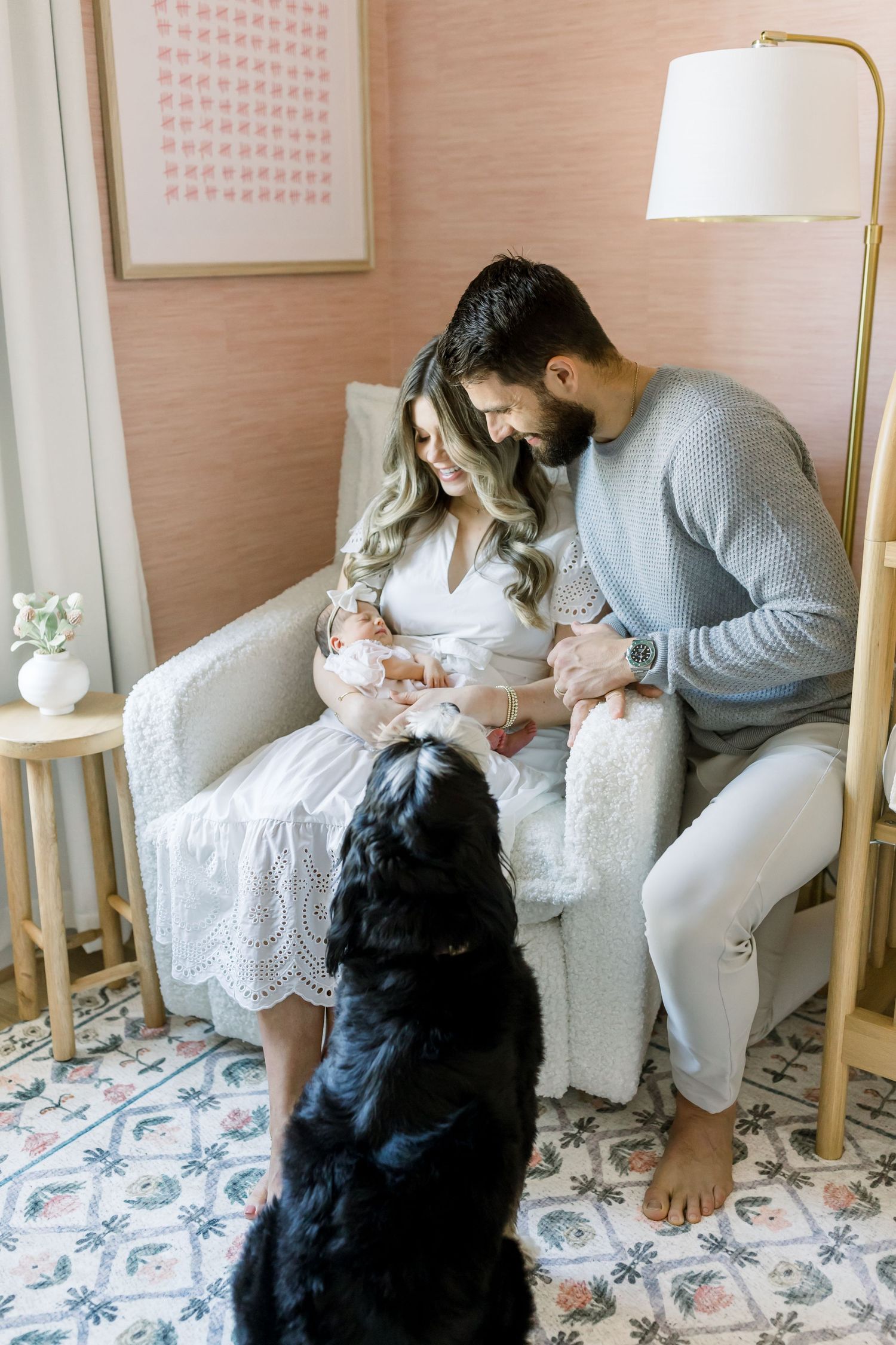 Intimate family moment in pink nursery with black dog watching from floor.
