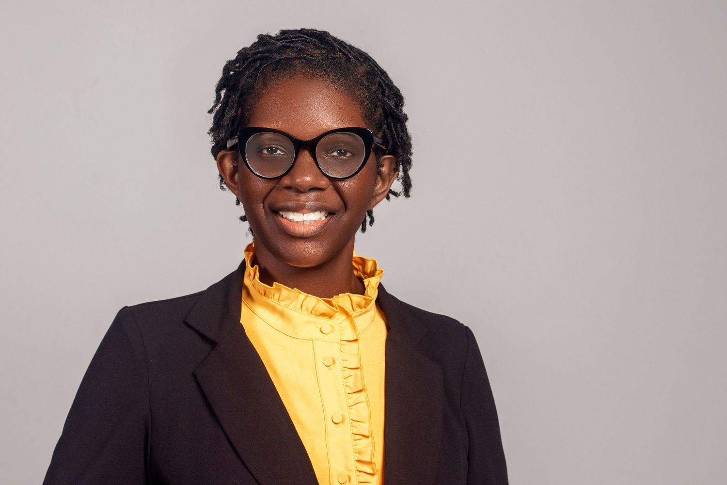 Professional headshot of person in black blazer and yellow ruffled shirt.