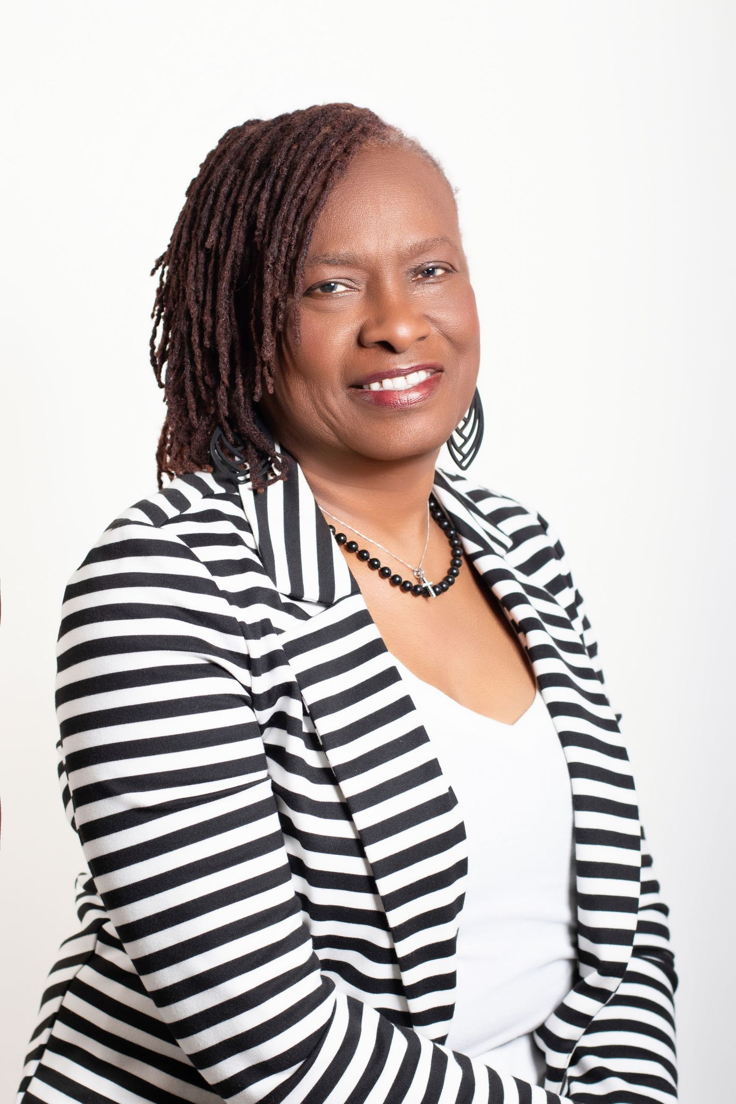 Professional portrait featuring a warm smile and stylish black and white striped blazer against a white background.