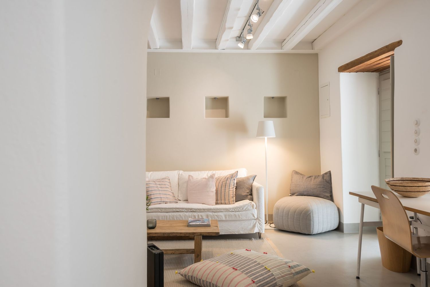 Modern minimalist living room with white walls, cozy daybed, pouf, and warm ambient lighting creating a serene atmosphere.