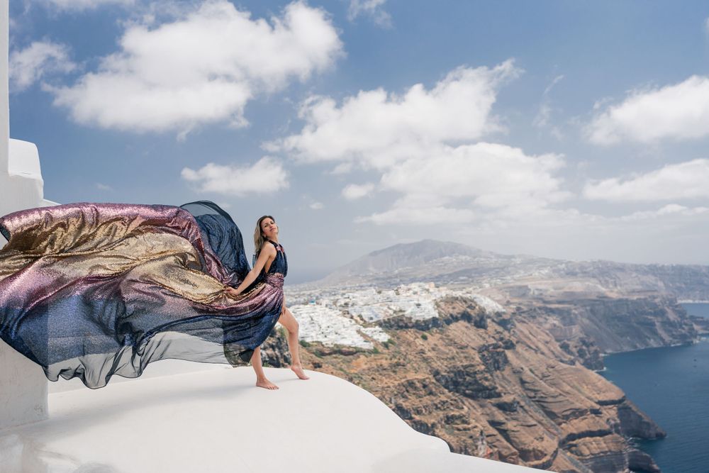 Dramatic fabric flowing in breeze atop white Santorini buildings overlooking azure sea.