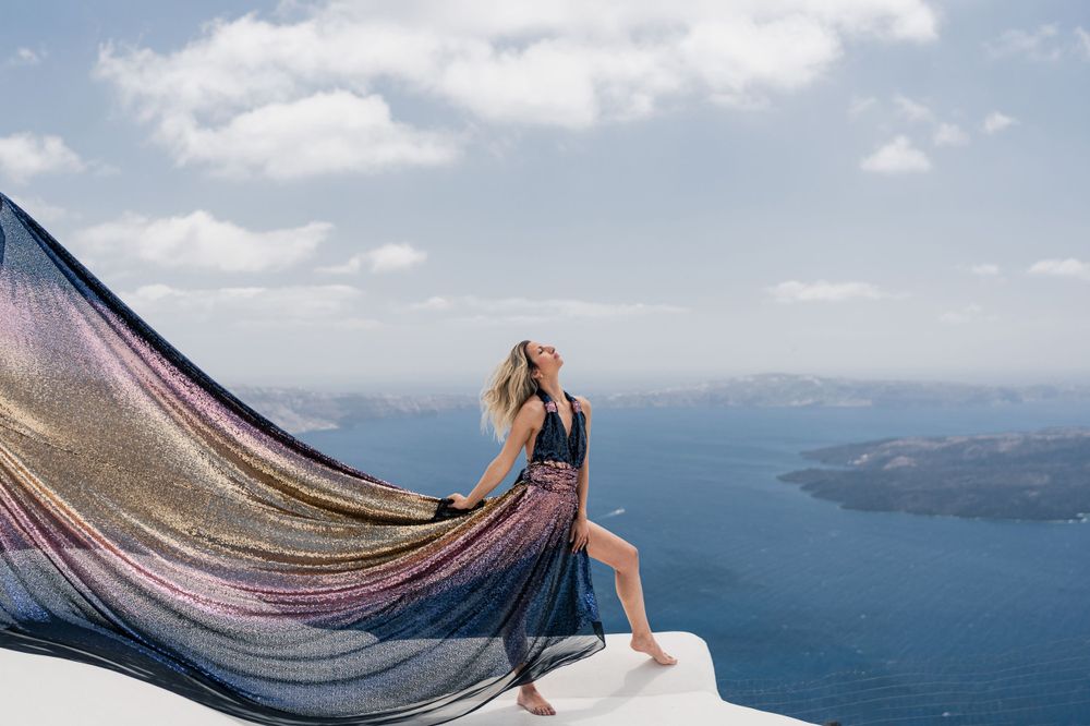 Sheer fabric flowing dramatically against blue Mediterranean backdrop on Santorini rooftop.