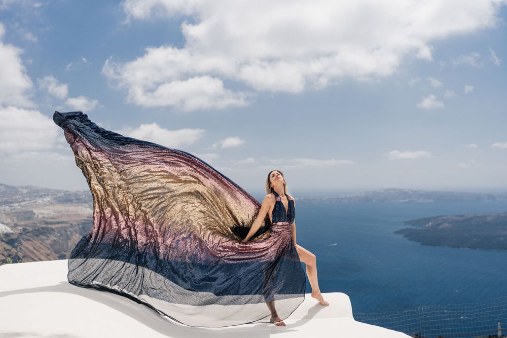 Ethereal dress fabric catching wind on white Santorini rooftop with sea views.