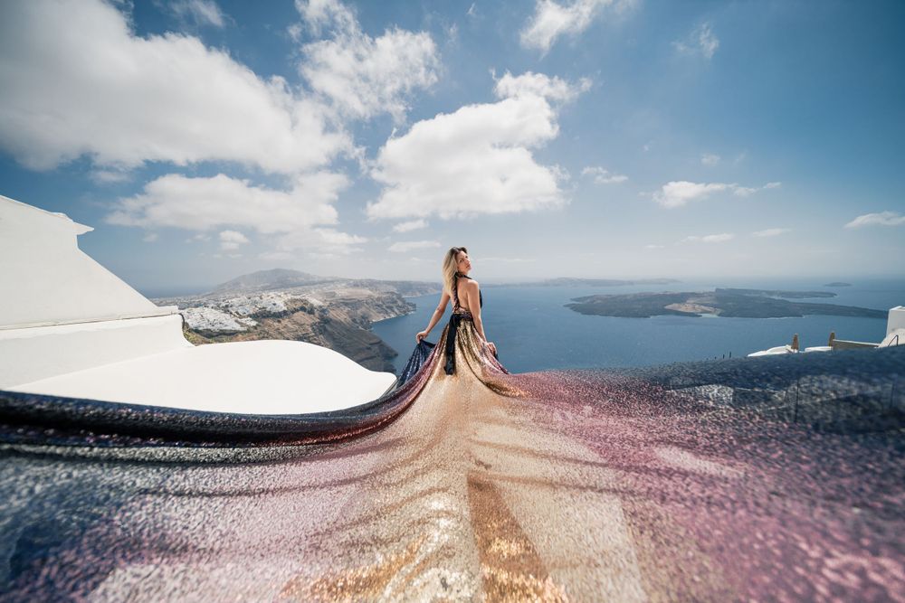 Flowing golden and pink dress fabric sweeps across Santorini's iconic white architecture.