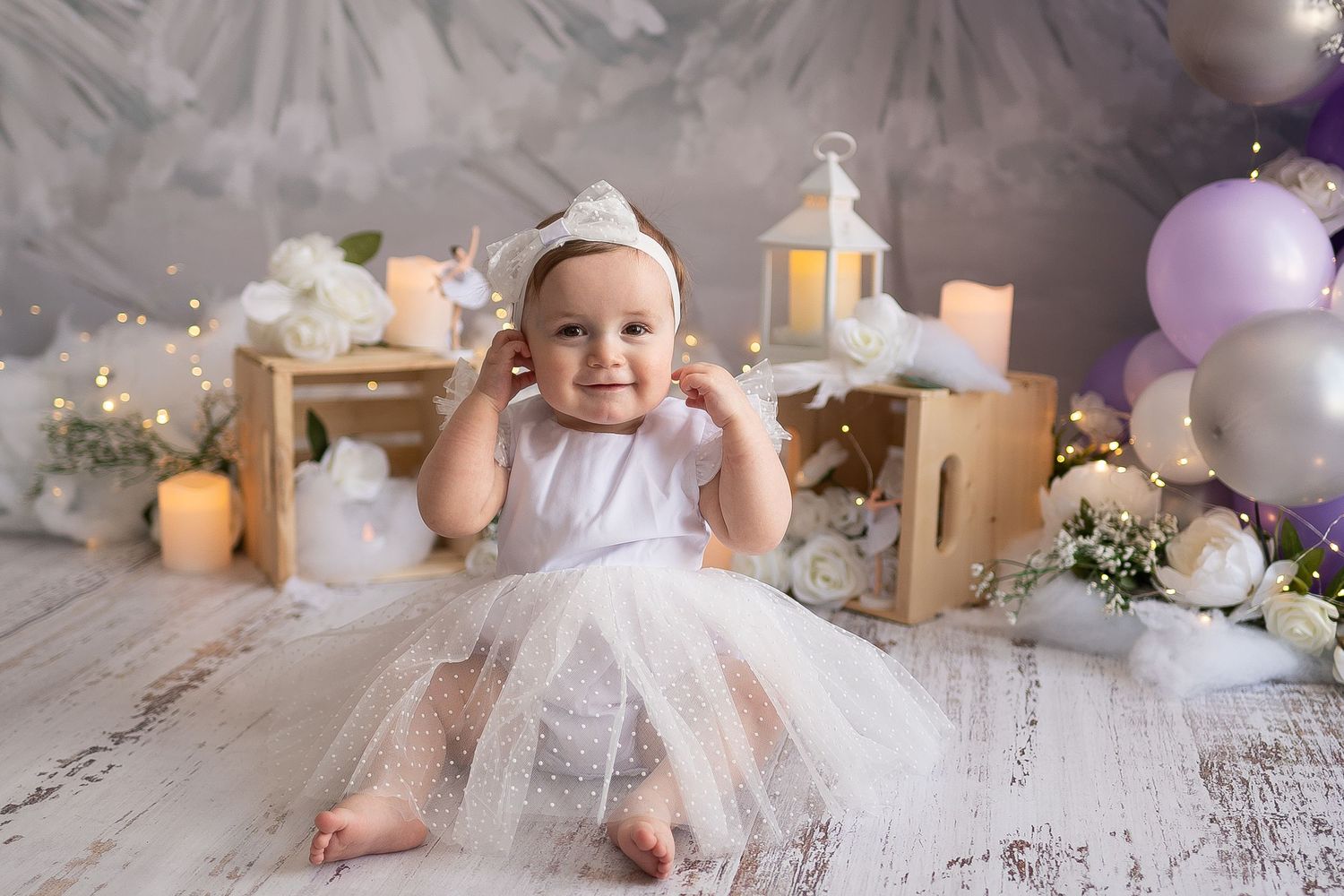 Baby in white tutu dress sitting among decorative lanterns and balloons.