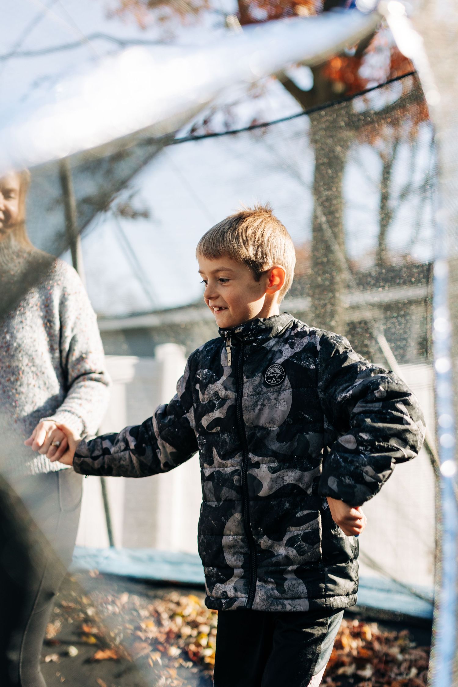 Child playing outside wearing camouflage jacket on sunny fall day.