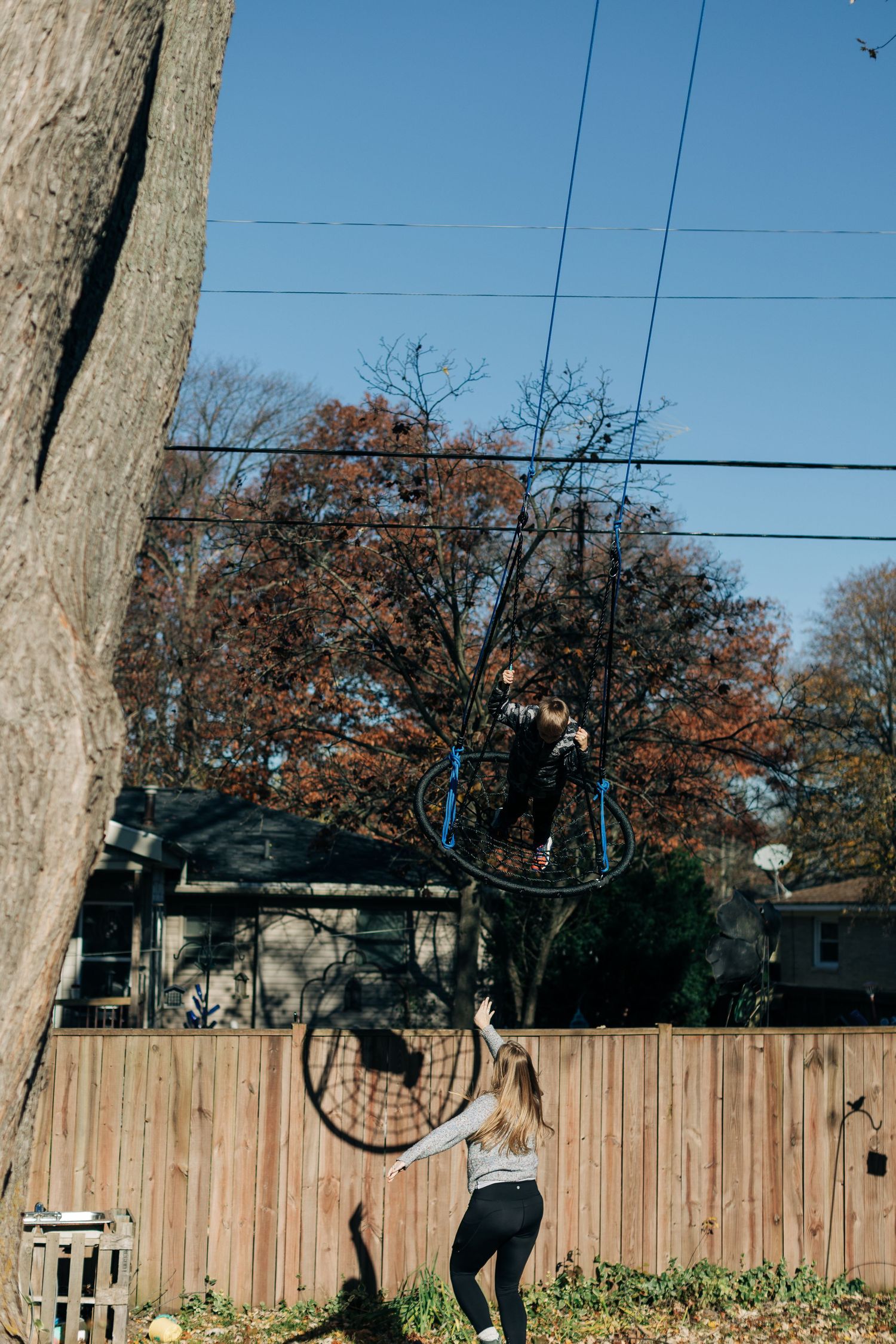 Person reaching up to touch rope swing against blue sky and autumn trees.