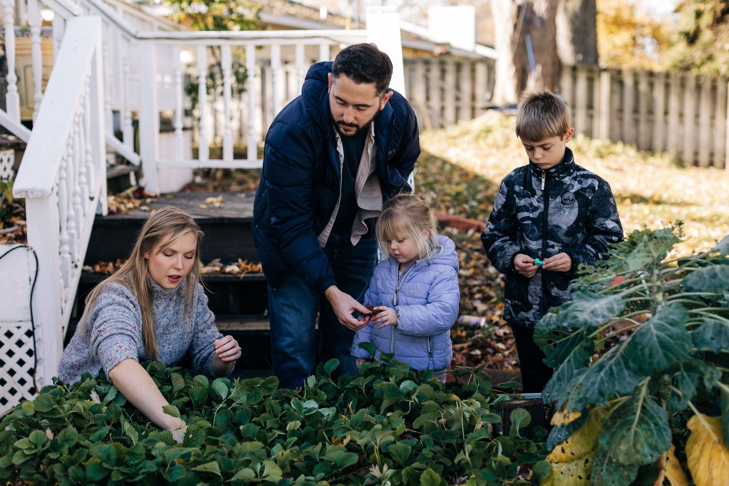 Family gathering in garden to examine plants and vegetables together.