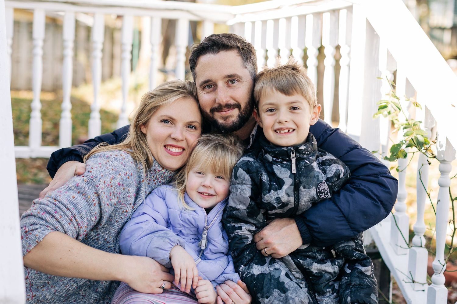 Family of four sitting together on white porch steps on a sunny day.