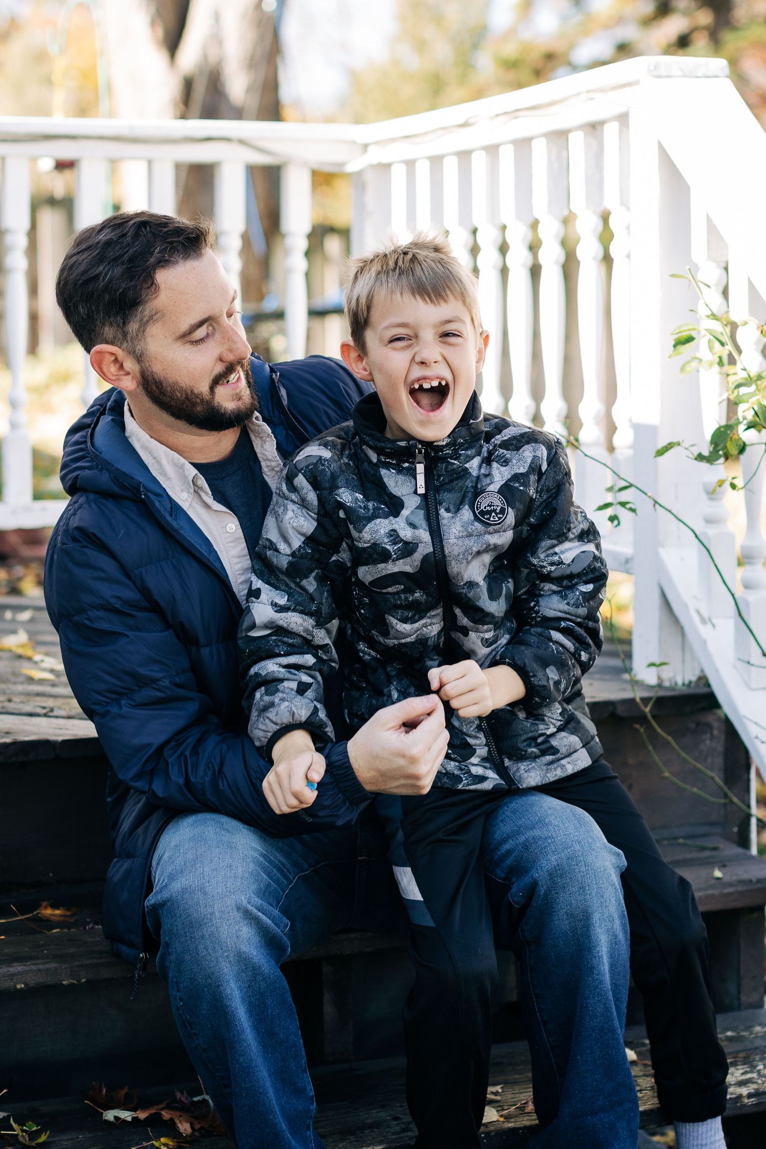 Father and son sharing a playful moment on white porch stairs outdoors.