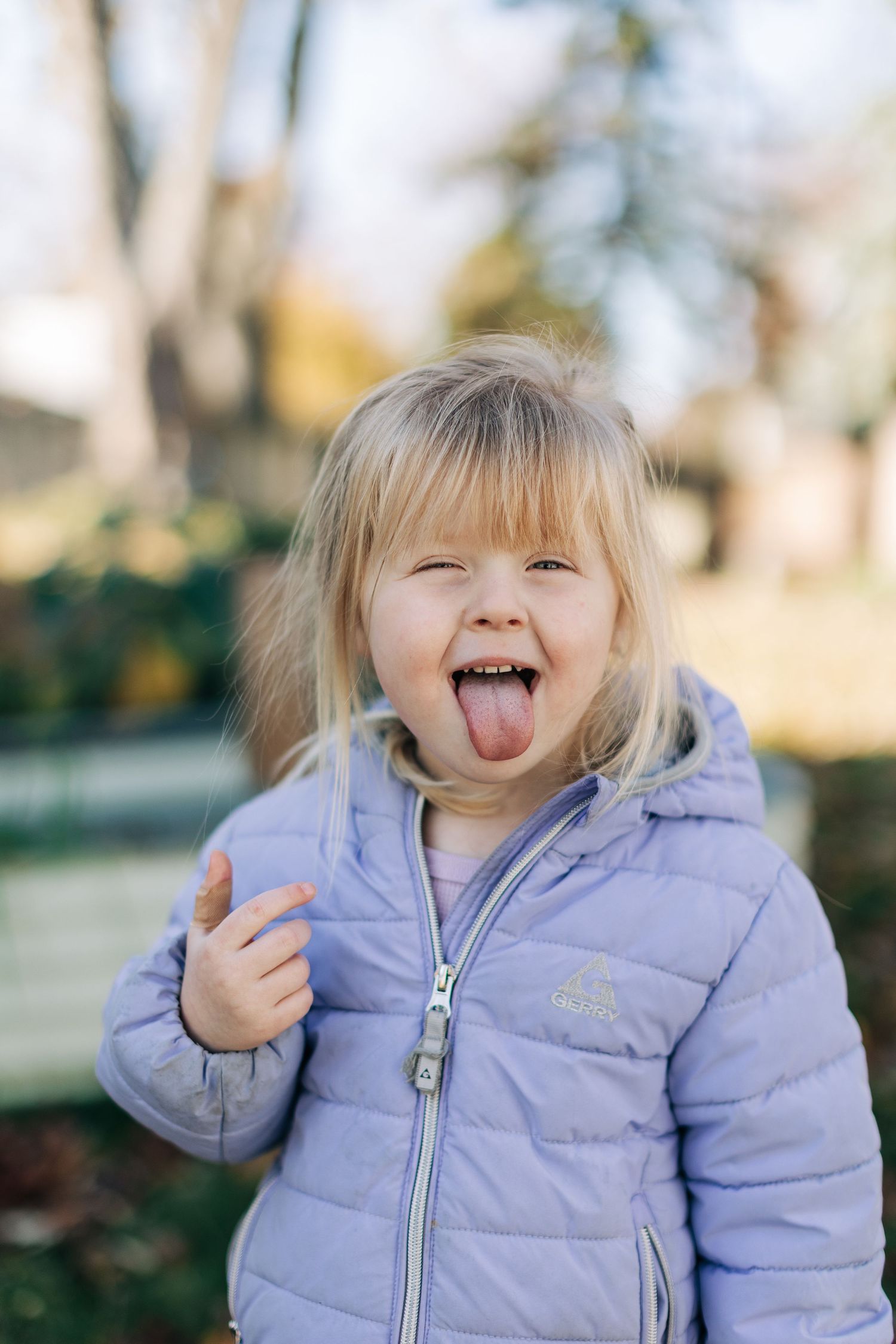 Young child in purple winter coat sticking tongue out playfully.