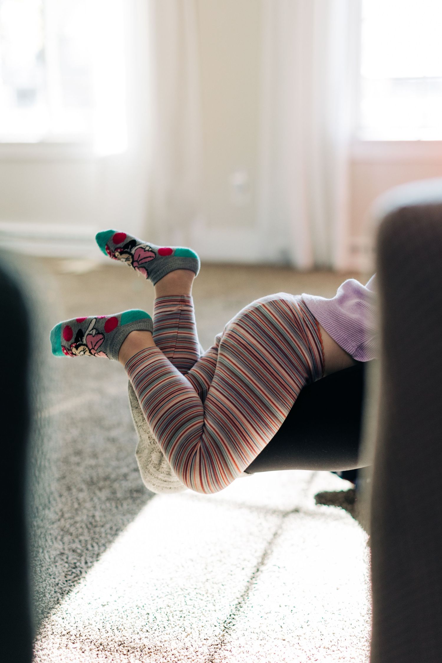 Striped leggings and colorful socks catching sunlight on carpet.