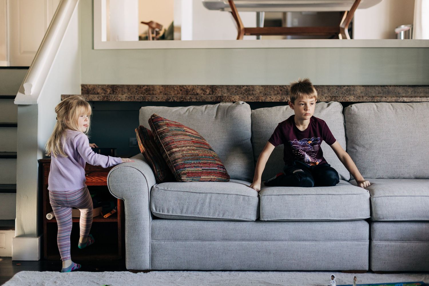 Two children playing near gray couch in modern living room.
