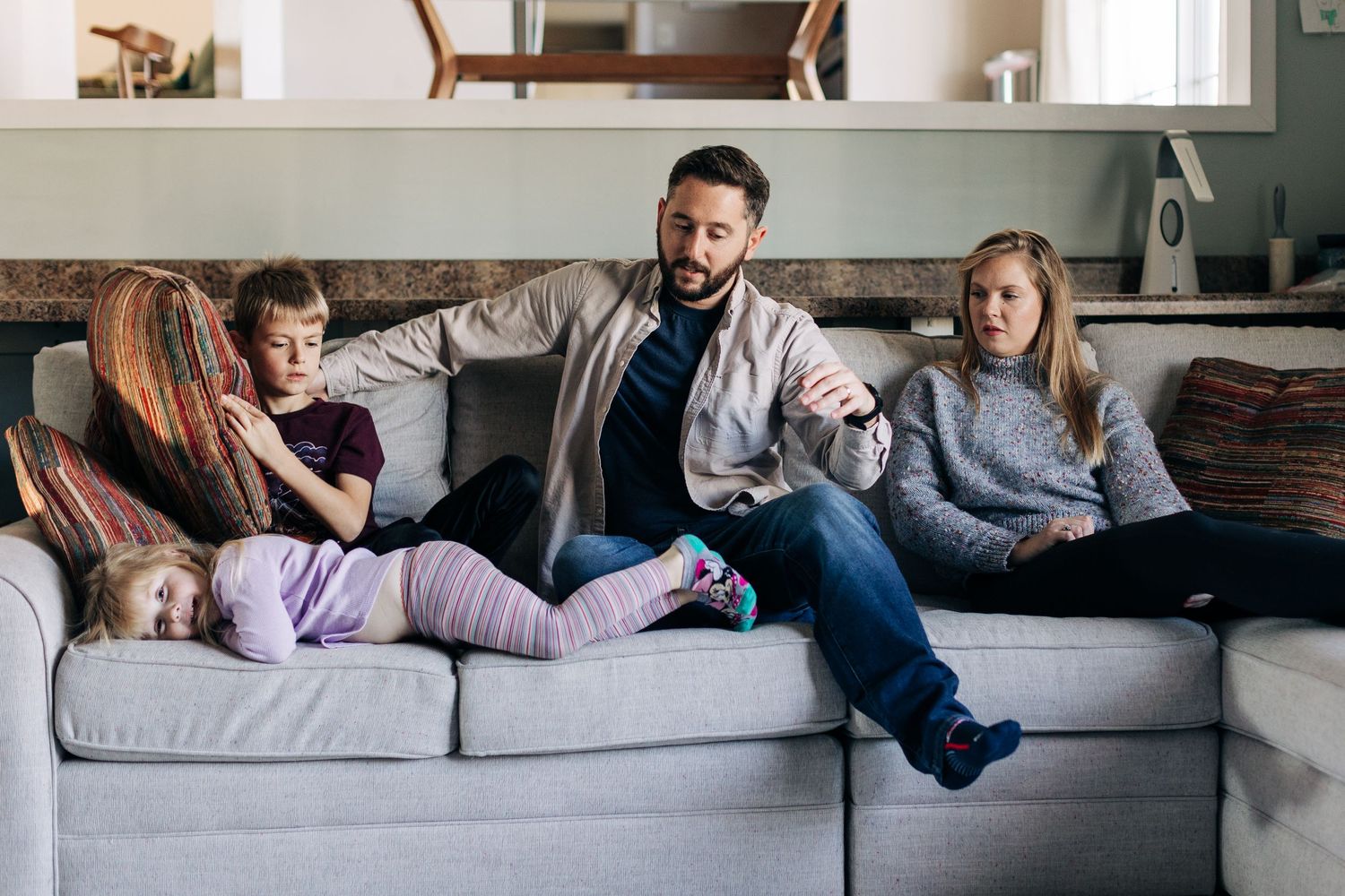 Family lounging together on gray sectional sofa in living room.