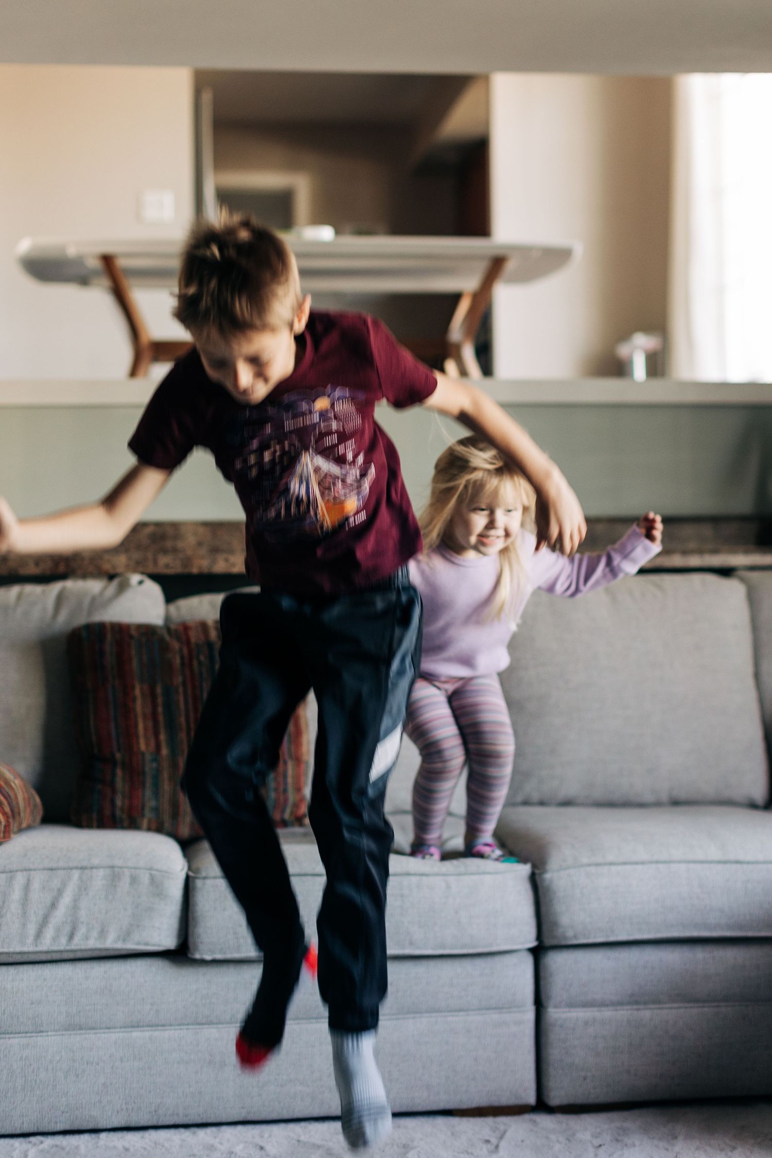 Children caught mid-jump while playing on a grey sectional sofa.