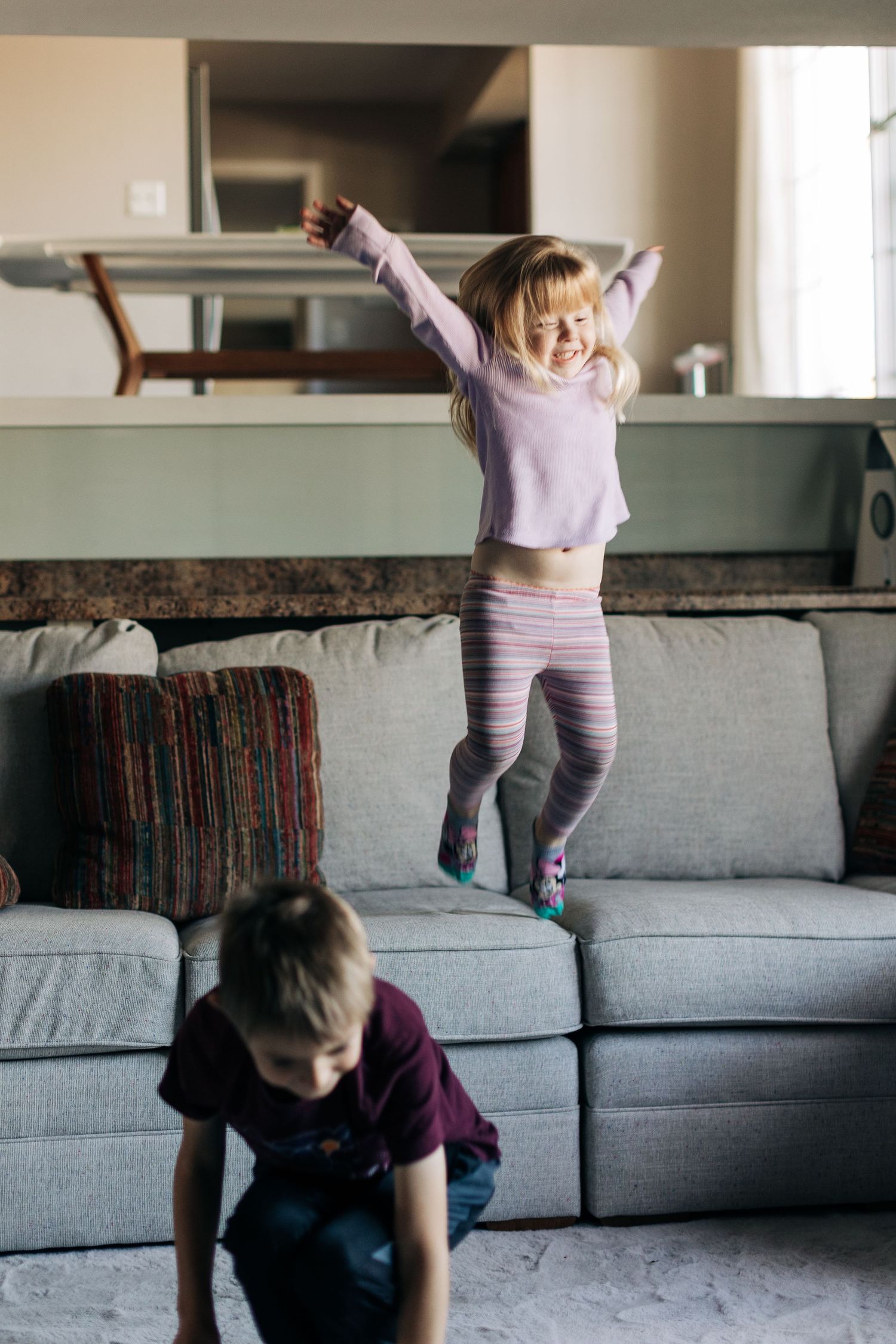 Playful kids jumping and having fun on a grey living room couch.