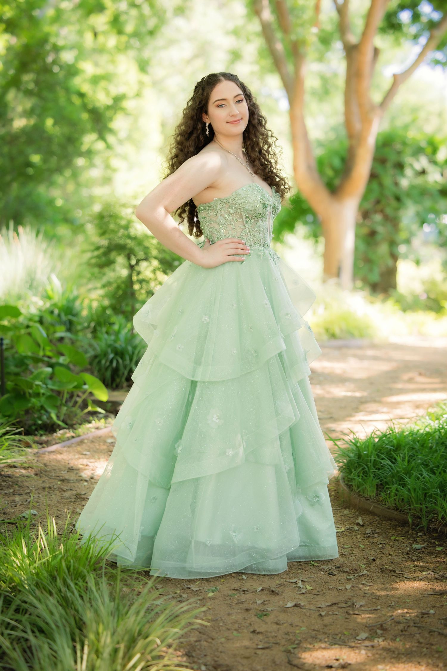 Young woman in a mint green ruffled ball gown posing elegantly in a sunlit outdoor garden setting in Grapevine, TX